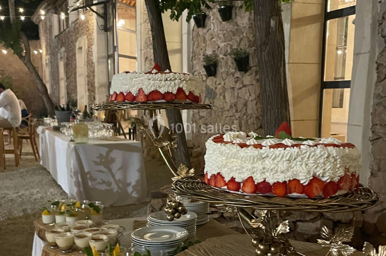 Deux gâteaux décorés de fraises sur des présentoirs dorés, entourés de desserts et d'une table dressée en extérieur.