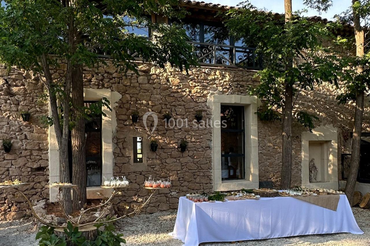 Façade en pierre d'une maison avec des arbres, une table dressée et des verres pour un événement en extérieur.