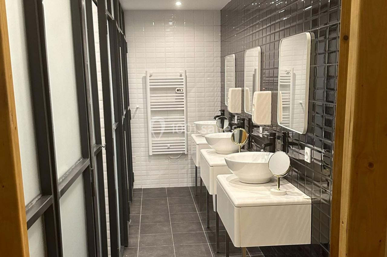 Salle de bain moderne avec trois lavabos, miroirs, carrelage noir et blanc, et un sèche-serviettes mural.