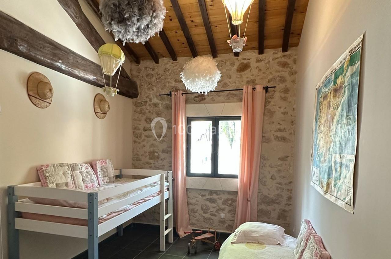 Chambre avec lits superposés, mur en pierre, plafond en bois, décorations aériennes et fenêtre avec rideaux roses.