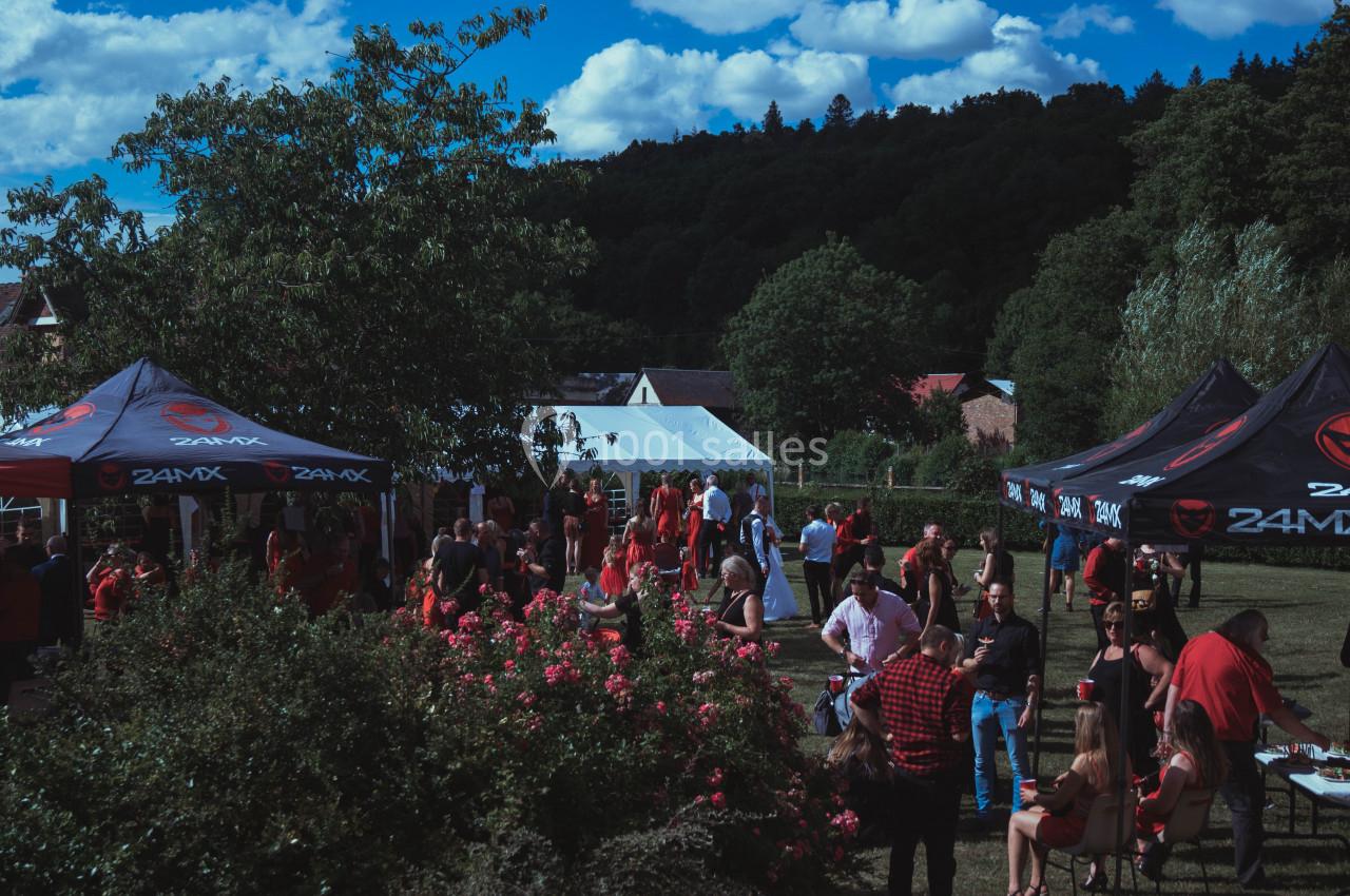 Groupe de personnes rassemblées dans un jardin avec des tentes, entourées de végétation et sous un ciel bleu.
