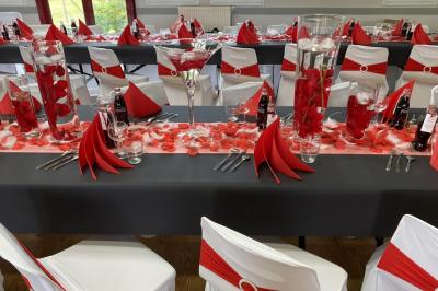 Salle décorée pour un événement avec des tables dressées en noir, rouge et blanc, et des chaises assorties.