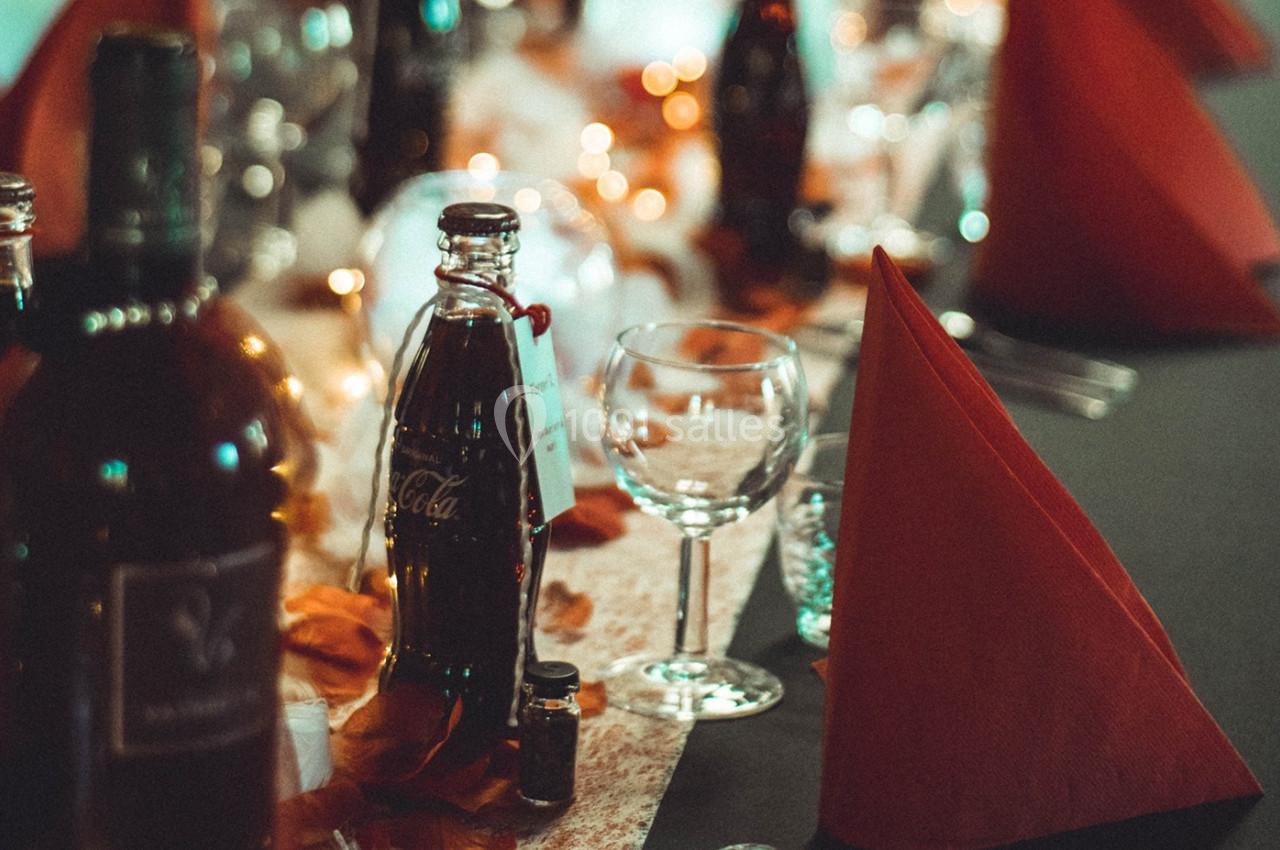 Table dressée avec des bouteilles, verres à pied, serviettes rouges pliées et décorations lumineuses.
