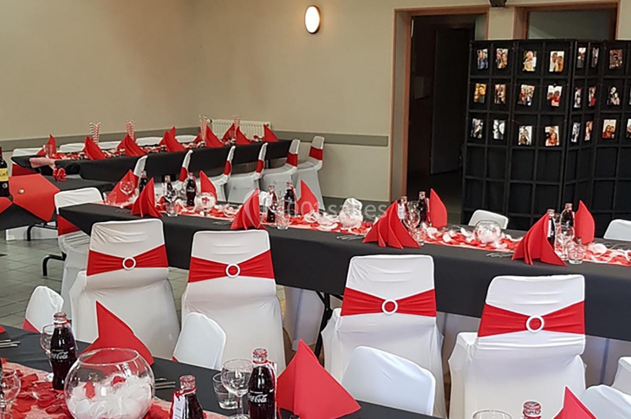 Salle décorée pour un événement avec des tables dressées en noir, rouge et blanc, et des chaises assorties.