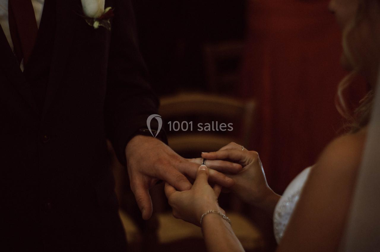 Une mariée passe une alliance au doigt du marié dans une ambiance tamisée.