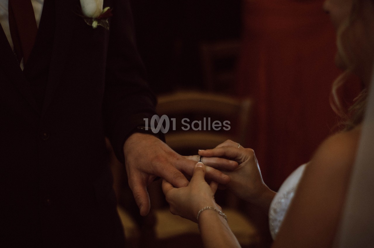 Une mariée passe une alliance au doigt du marié dans une ambiance tamisée.