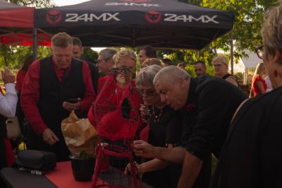 Salle décorée pour un événement avec des tables dressées en noir, rouge et blanc, et des chaises assorties.