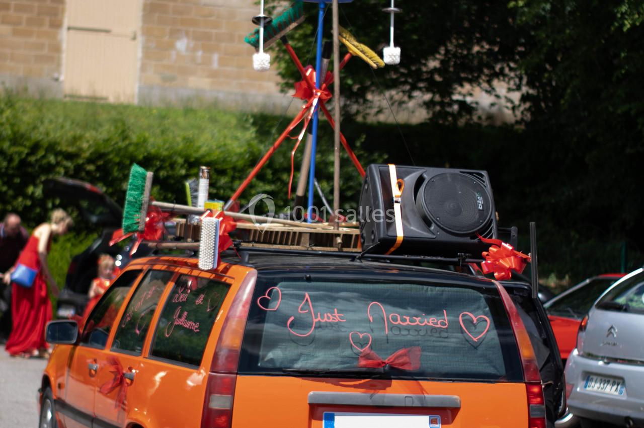 Voiture orange décorée pour un mariage avec des rubans, des accessoires et un message ’Just Married’ sur la vitre arrière.