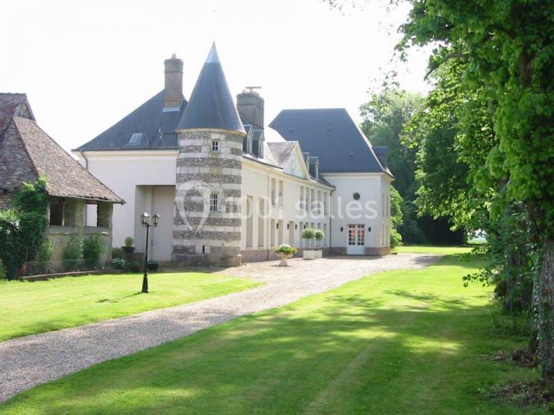 Grande maison de style traditionnel avec tour en pierre, allée gravillonnée et jardin verdoyant.