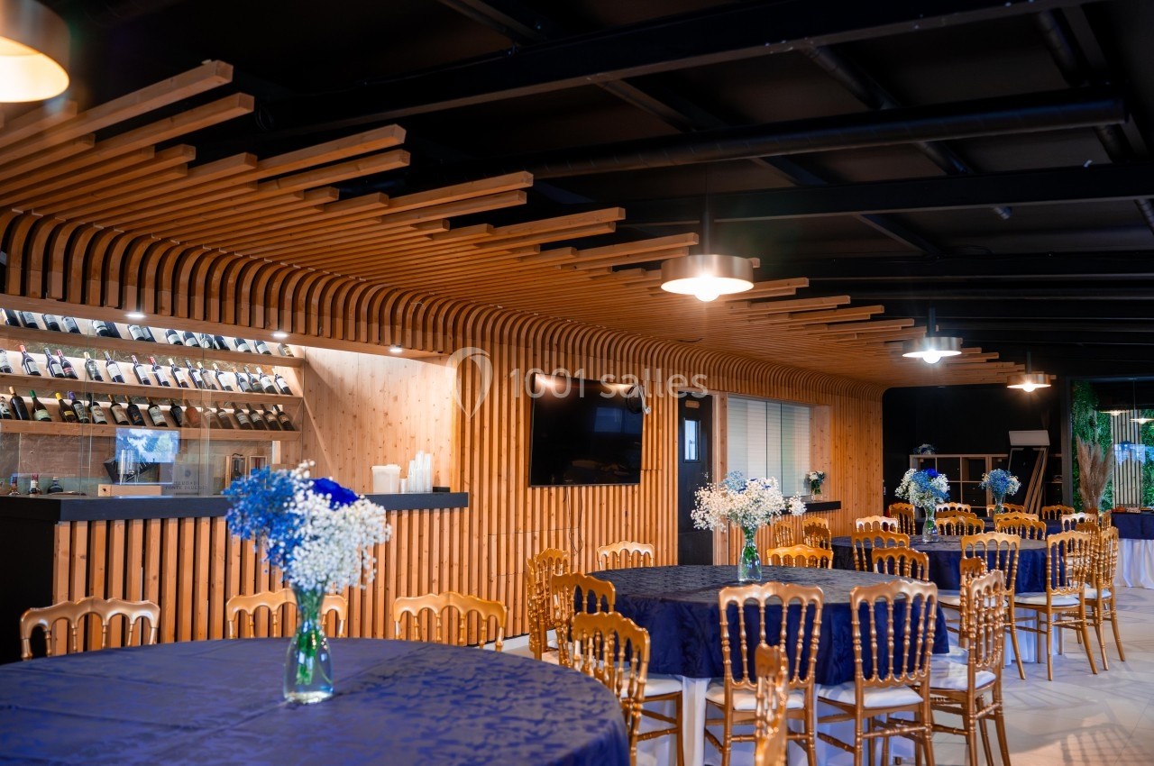Salle moderne avec tables rondes couvertes de nappes bleues, chaises en bois doré et décoration florale, éclairage…