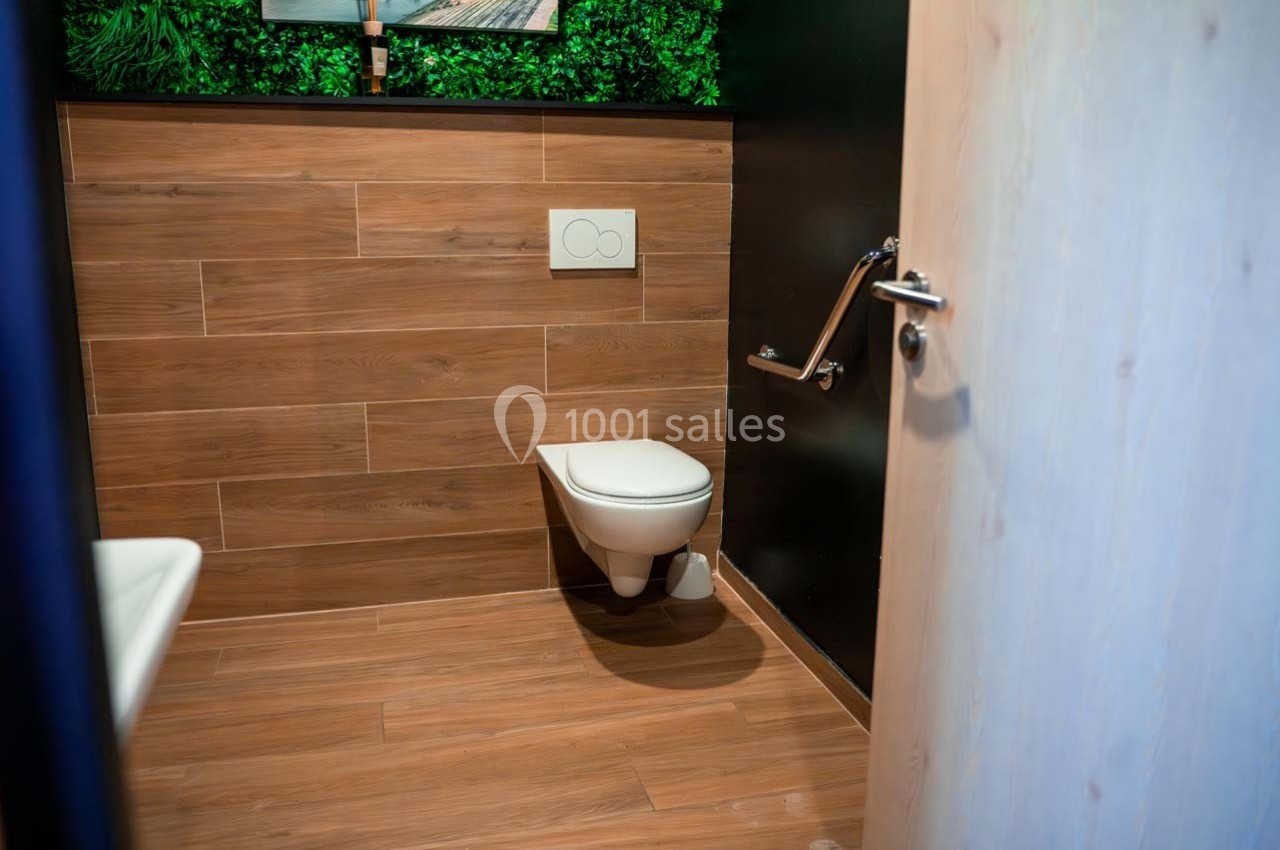 Toilettes modernes avec cuvette suspendue, mur en bois, barre d'appui et porte entrouverte.