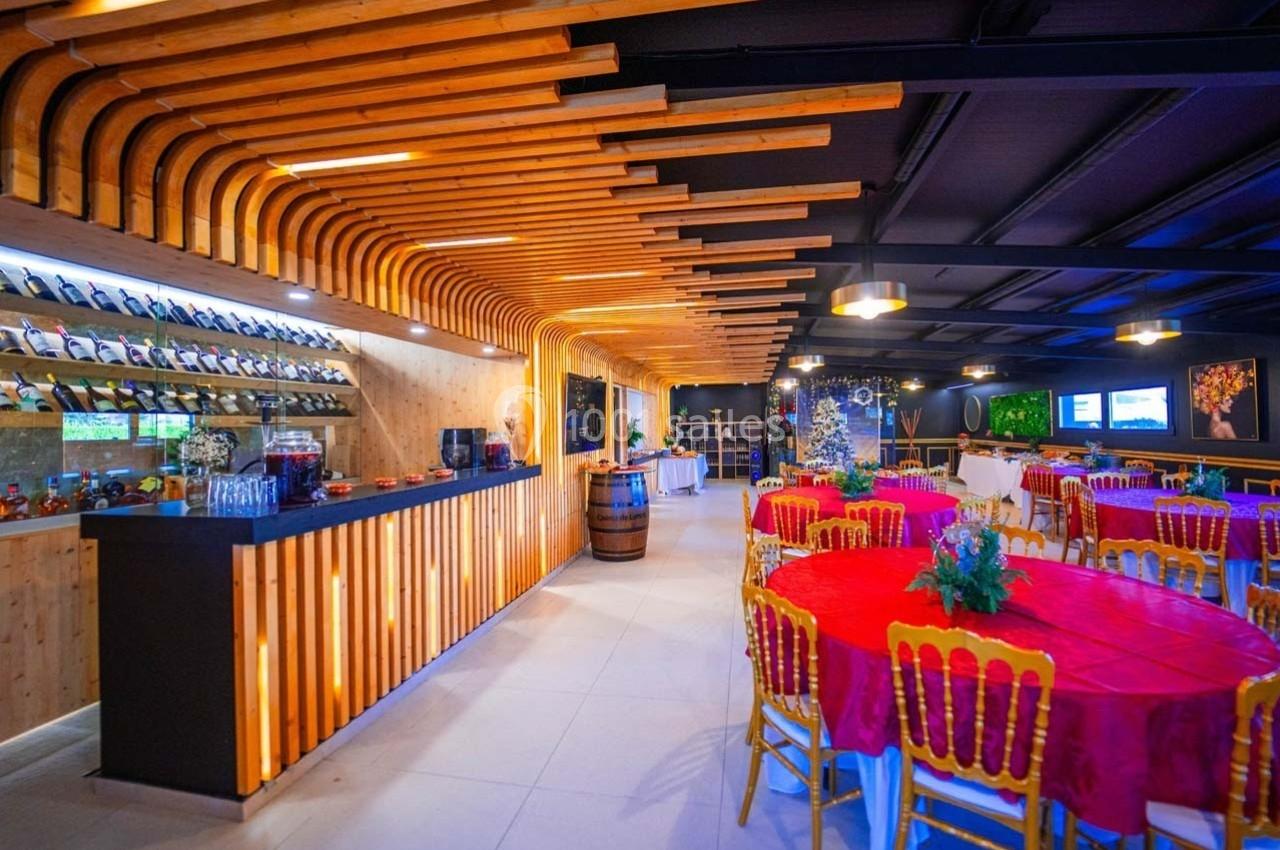 Salle de réception avec tables rondes dressées de nappes rouges, bar en bois et décoration lumineuse moderne.