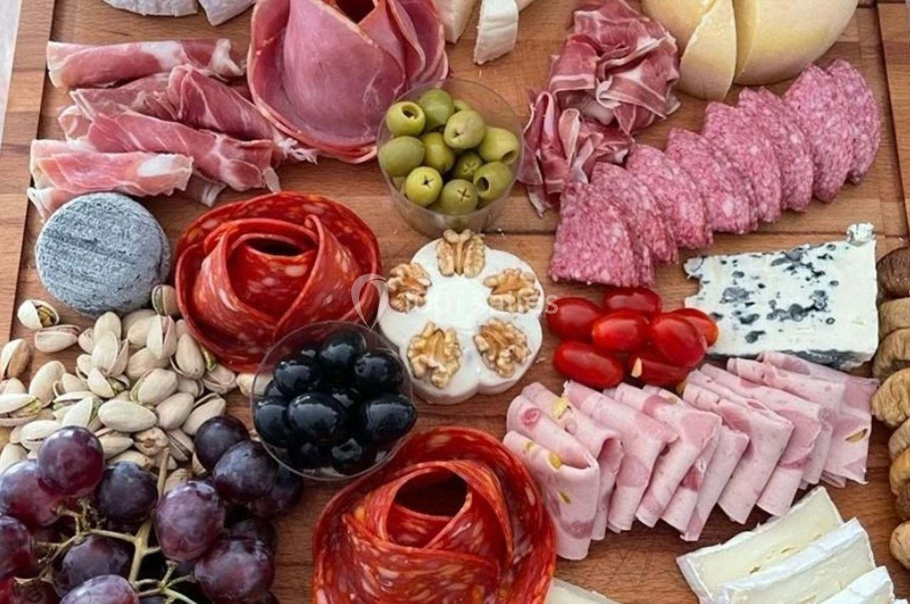 Plateau de charcuterie et fromages variés avec fruits, noix, olives et pistaches disposés sur une planche en bois.