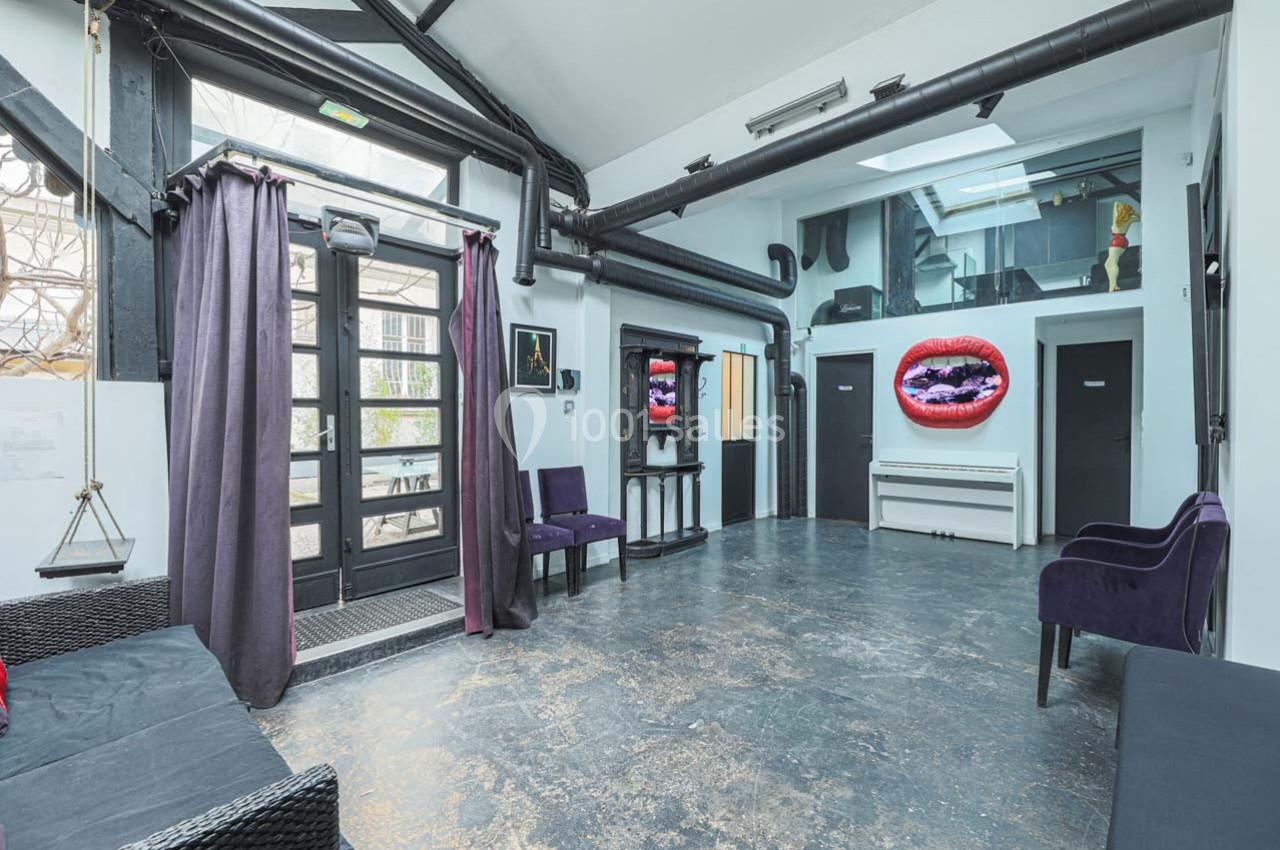 Salle lumineuse avec sol en béton, mobilier minimaliste, grandes fenêtres et une œuvre d'art représentant des lèvres rouges.