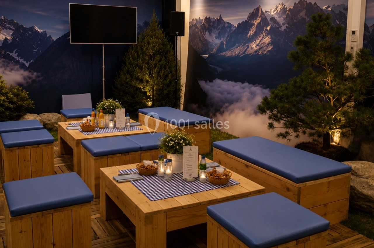 Espace extérieur aménagé avec des bancs et tables en bois, décoré de plantes et éclairé dans une ambiance montagnarde.
