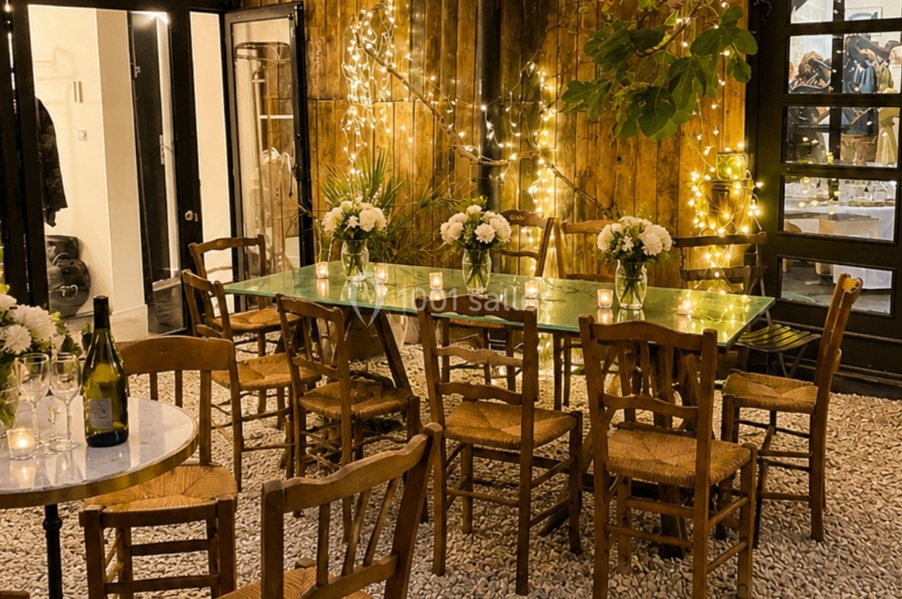 Terrasse éclairée par des guirlandes lumineuses, avec tables en bois, chaises en paille et vases de fleurs blanches.