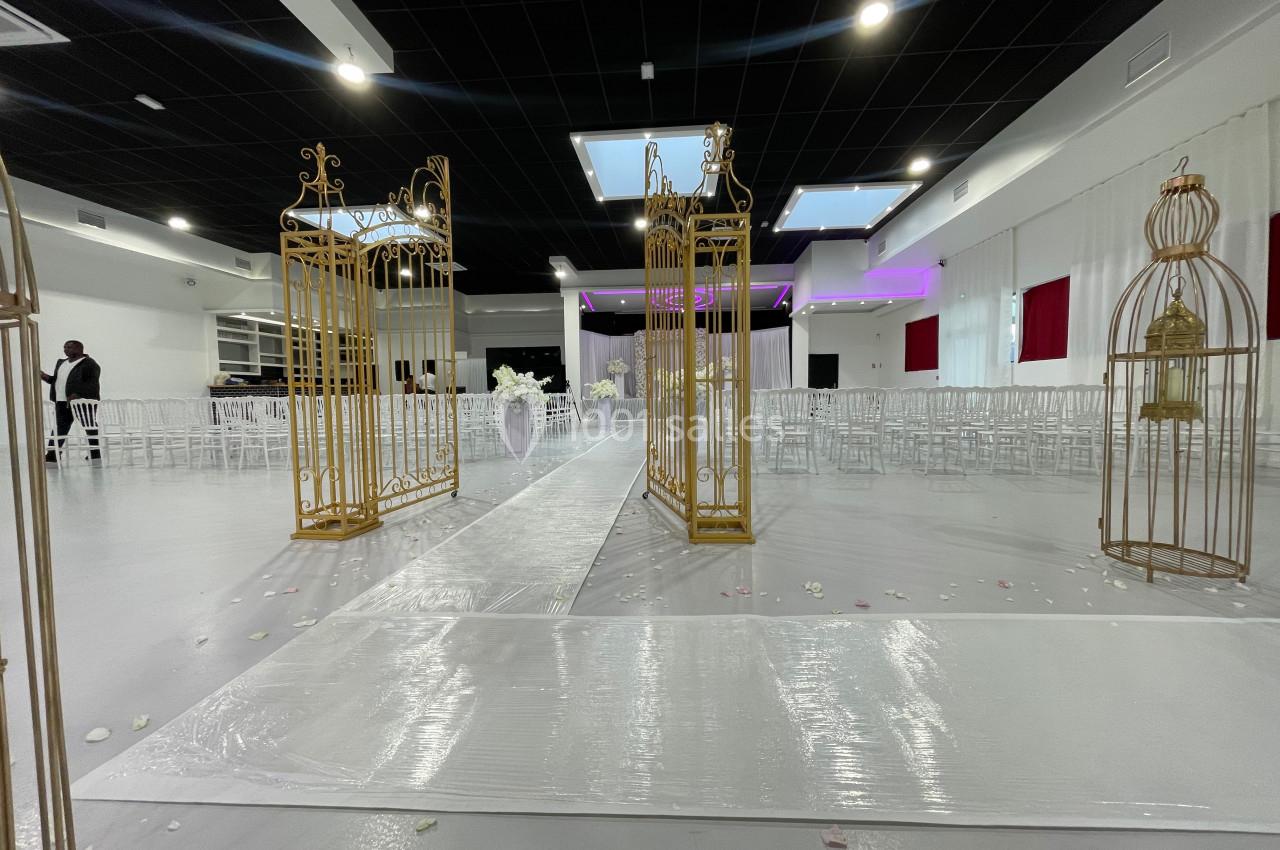 Allée centrale décorée de cages dorées dans une salle de réception avec chaises blanches et éclairage tamisé.