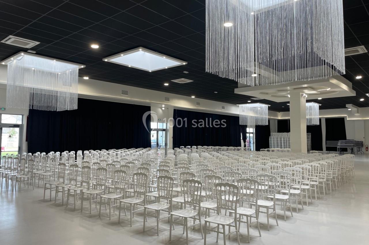 Salle de réception avec des rangées de chaises blanches alignées sous un plafond décoré de fils suspendus.