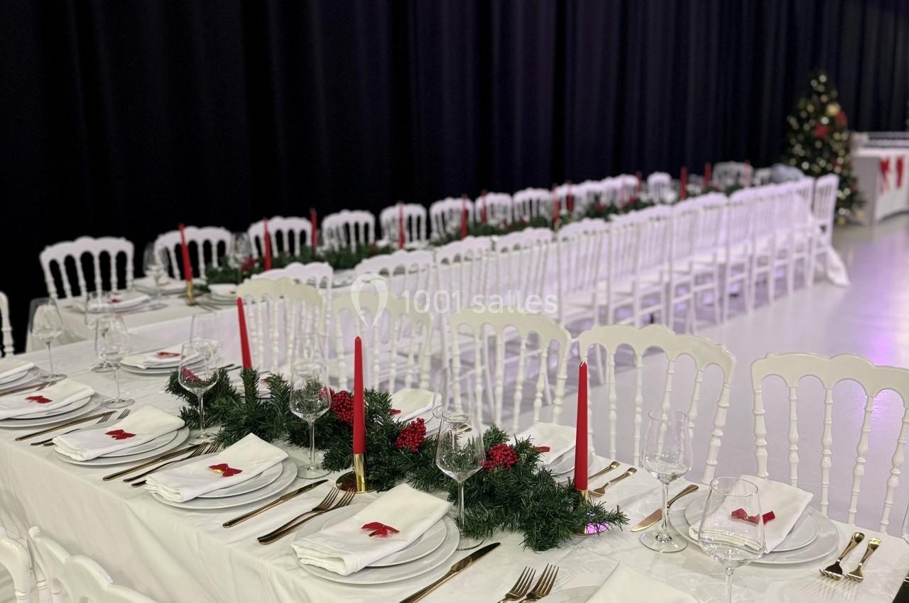 Tables de banquet décorées avec nappes blanches, bougies rouges, couverts dorés et guirlandes, dans une salle sombre.