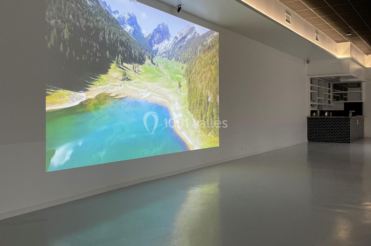 Projection d'un paysage de montagne avec lac turquoise sur un mur blanc dans une pièce moderne et épurée.