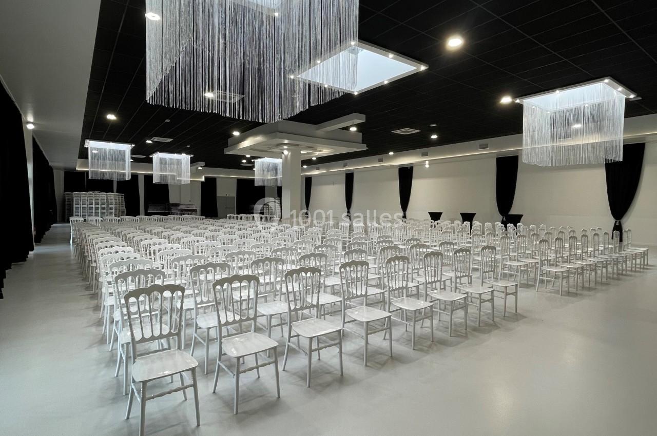 Salle de réception moderne avec rangées de chaises blanches alignées sous des luminaires suspendus.