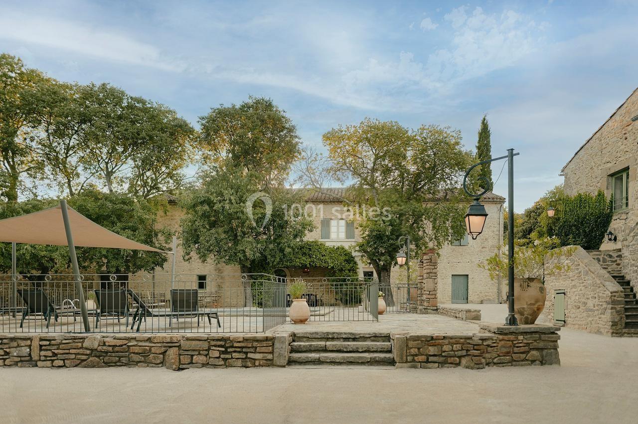 Cour extérieure en pierre avec piscine clôturée, mobilier de jardin, arbres et bâtiments en arrière-plan.