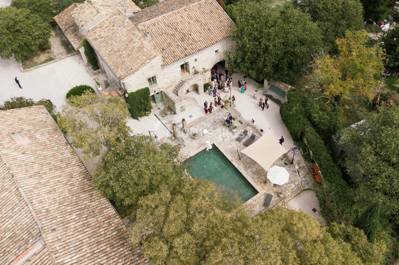 Vue aérienne d'un domaine en pierre avec une cour centrale, une piscine et des invités rassemblés autour.