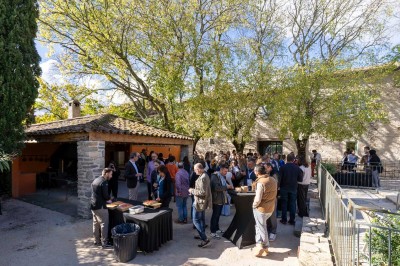 Vue aérienne d'une grande maison en pierre avec piscine, entourée de forêts et de champs sous un ciel dégagé.