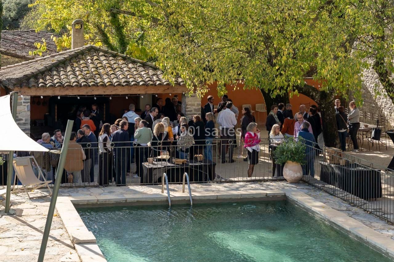 Groupe de personnes réunies près d'une piscine dans une cour extérieure avec arbres et bâtiment en pierre.