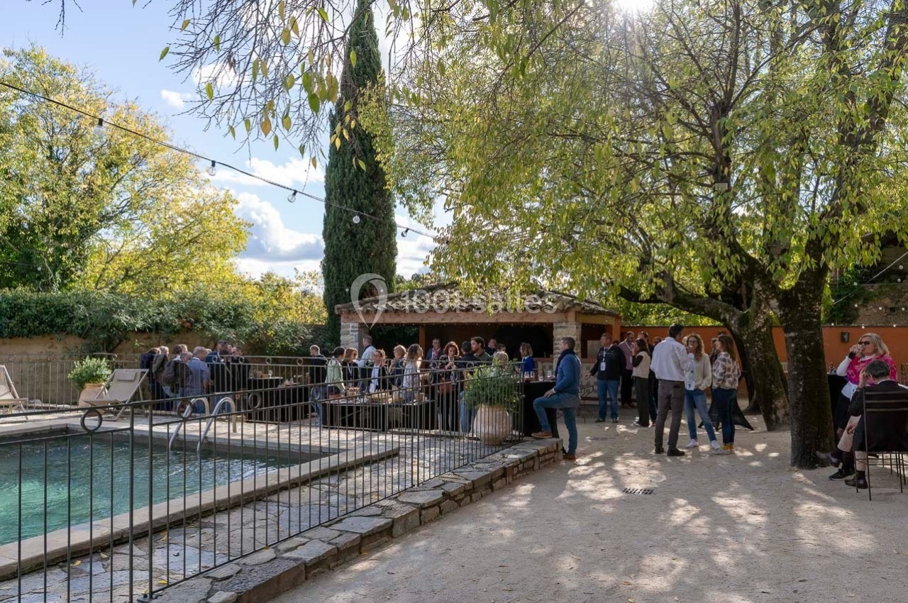 Groupe de personnes réunies près d'une piscine dans un jardin arboré, sous une lumière naturelle.