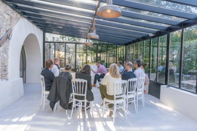 Vue aérienne d'une grande maison en pierre avec piscine, entourée de forêts et de champs sous un ciel dégagé.