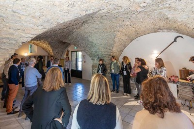 Vue aérienne d'une grande maison en pierre avec piscine, entourée de forêts et de champs sous un ciel dégagé.