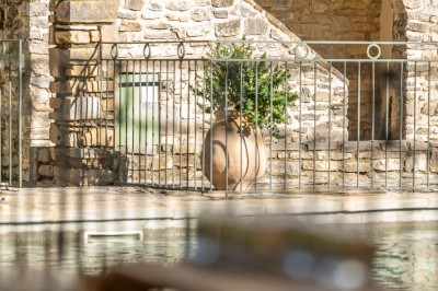 Vue aérienne d'une grande maison en pierre avec piscine, entourée de forêts et de champs sous un ciel dégagé.