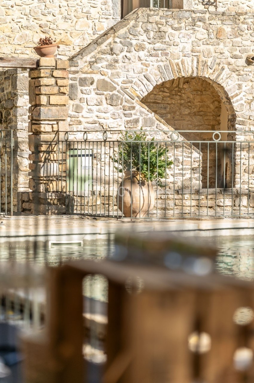 Façade en pierre avec une arche, une jarre décorative et une balustrade métallique, vue depuis un espace extérieur.