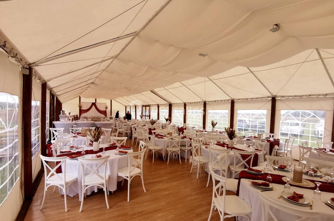 Salle de réception sous chapiteau avec tables dressées, nappes blanches et décorations rouges.