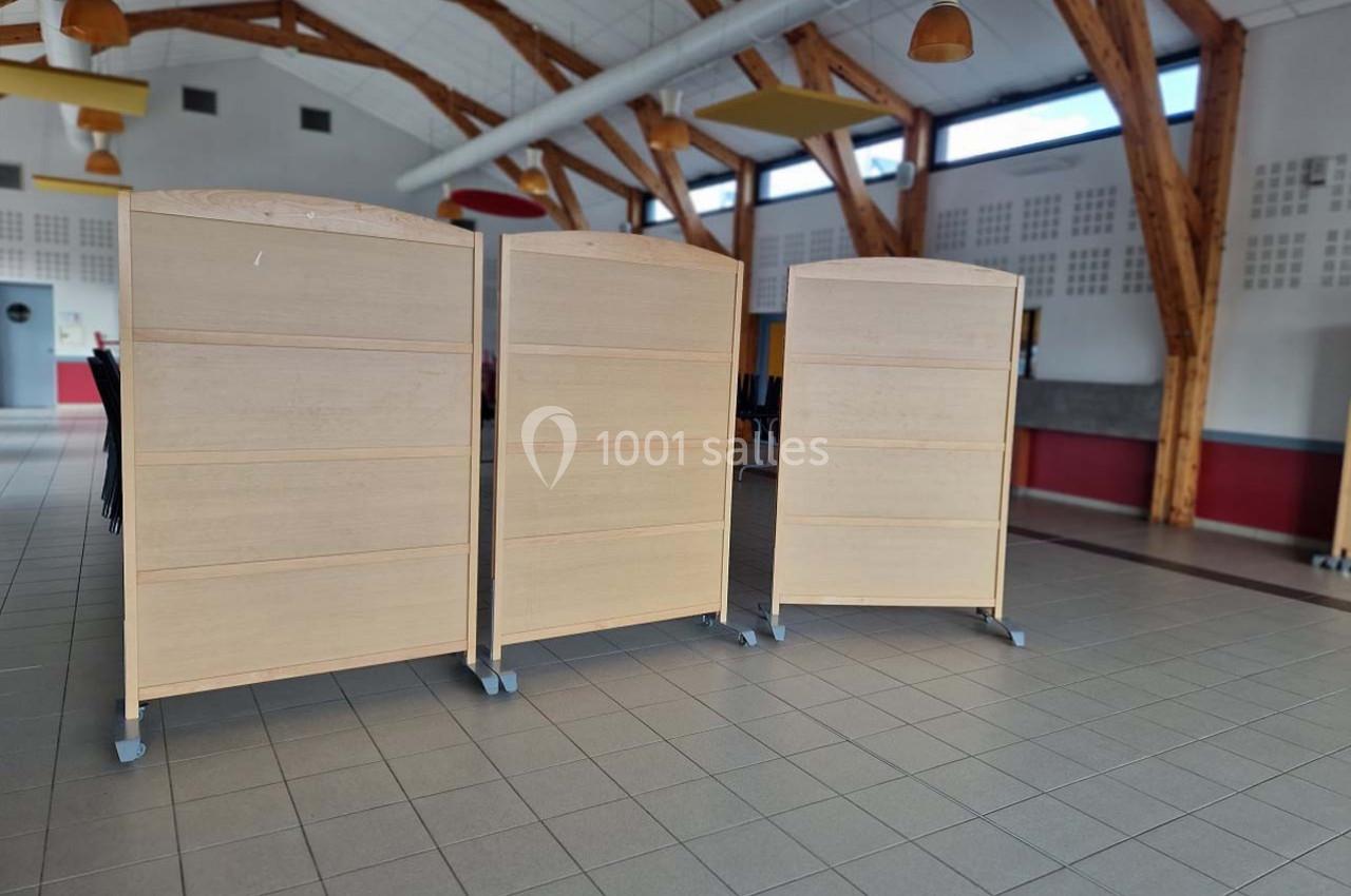 Trois panneaux en bois sur roulettes disposés dans une grande salle lumineuse avec charpente apparente.
