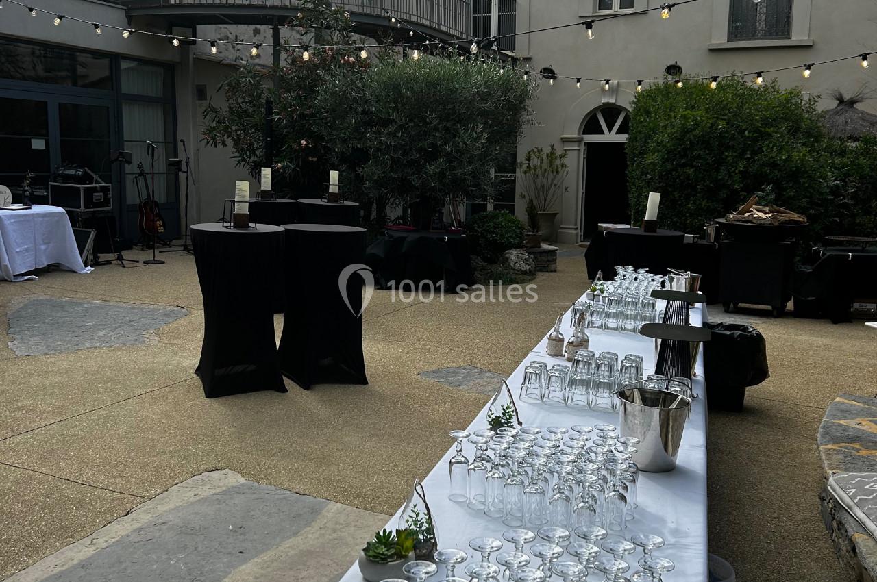 Table dressée avec des verres et des seaux à glace dans une cour extérieure, entourée de bâtiments et d'arbres.