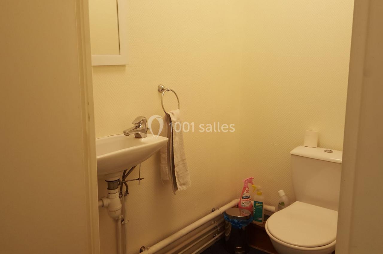 Petite salle de bain avec lavabo, miroir, toilettes, produits de nettoyage et porte-serviettes mural.