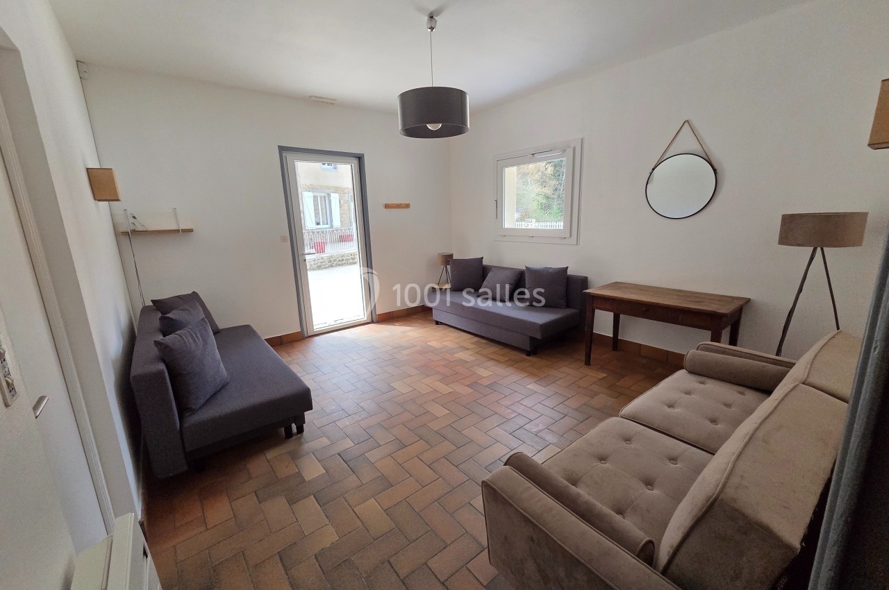 Salon lumineux avec trois canapés, un miroir rond, une table en bois et un sol en carrelage.