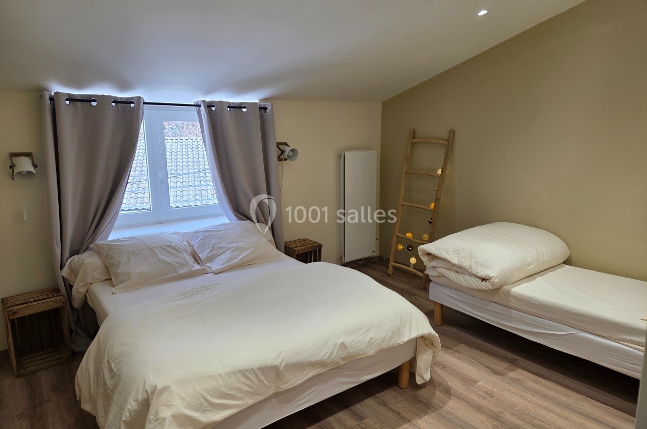 Chambre lumineuse avec un lit double, un lit simple, des rideaux beiges, un sol en bois et une échelle décorative.