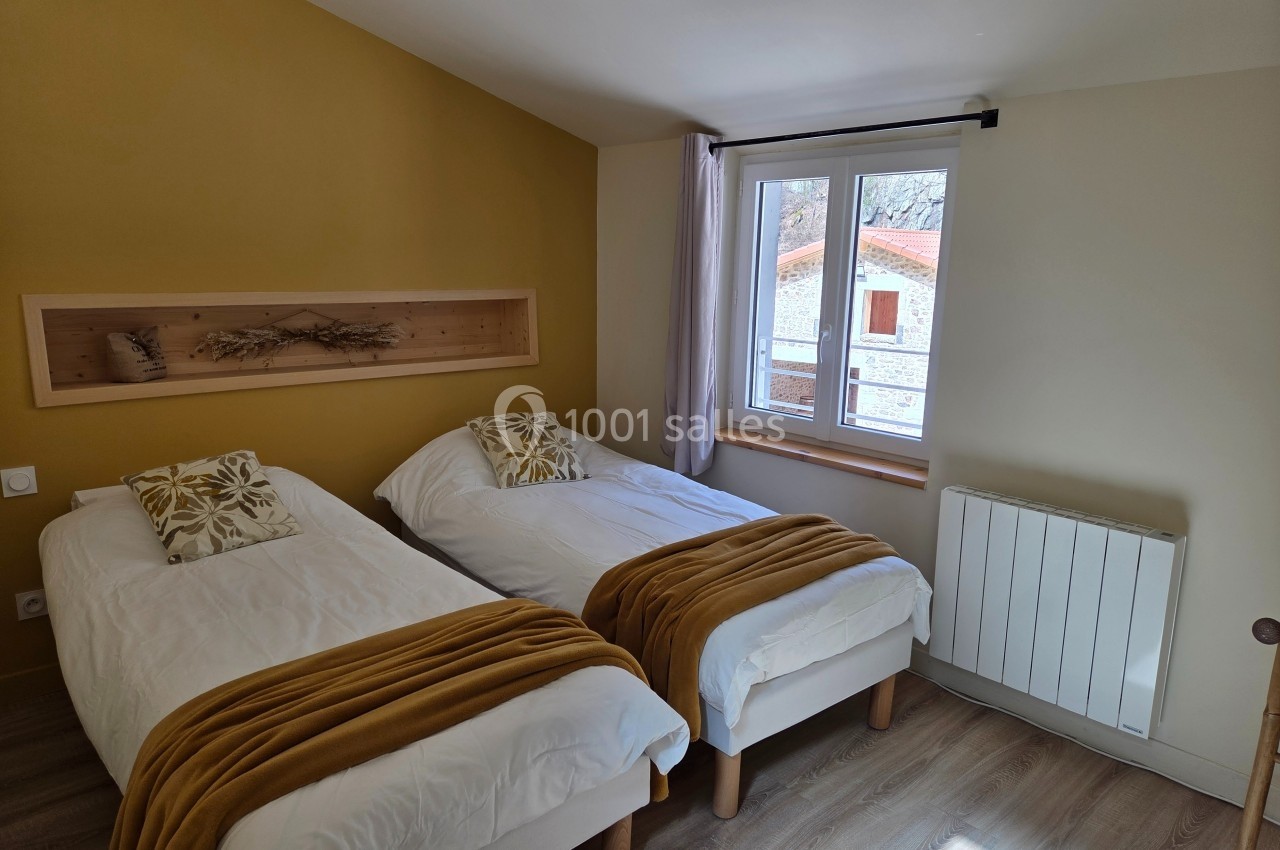 Chambre avec deux lits simples, couvertures jaunes, mur jaune, fenêtre donnant sur un bâtiment extérieur.