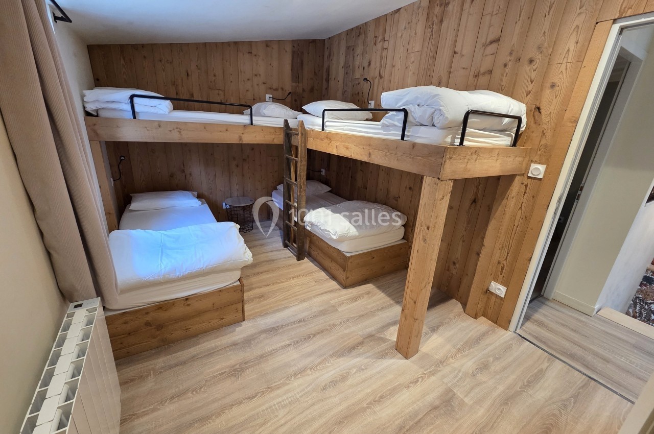 Chambre avec lits superposés en bois, parquet clair, murs en bois et porte ouverte sur une autre pièce.
