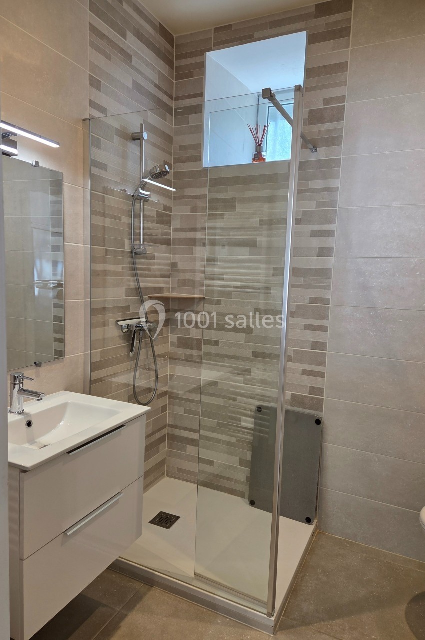 Salle de bain moderne avec douche à l'italienne, paroi vitrée, meuble vasque blanc et carrelage beige et marron.