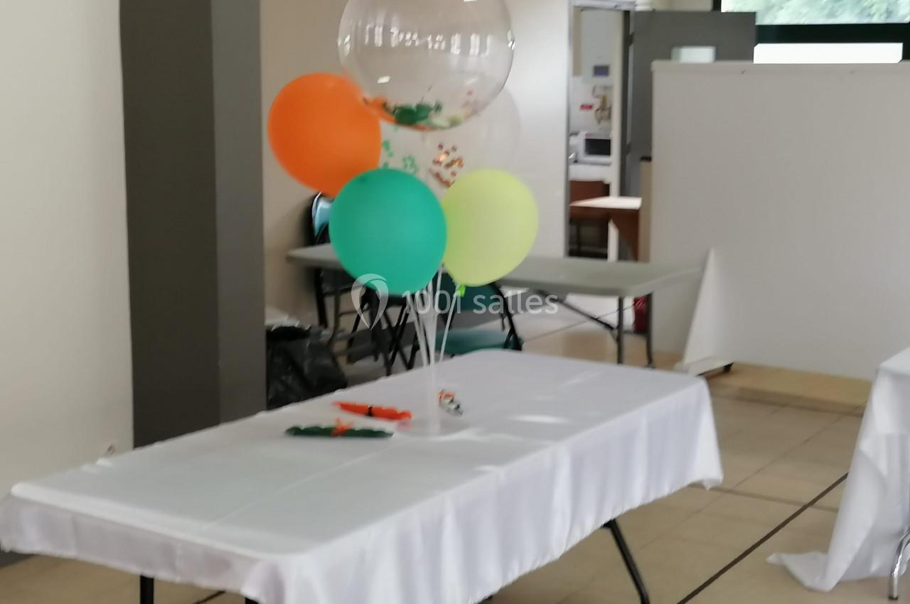 Table décorée avec des ballons colorés et une nappe blanche dans une salle lumineuse.