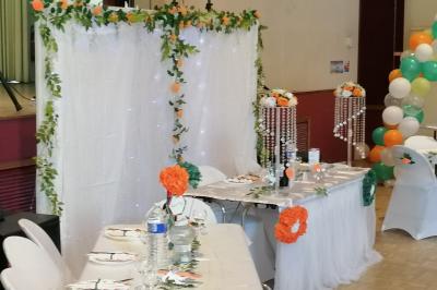 Serviettes pliées en forme de fleurs, orange et bleue, disposées sur des verres transparents sur une table en bois.