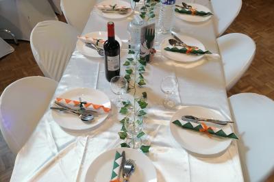 Serviettes pliées en forme de fleurs, orange et bleue, disposées sur des verres transparents sur une table en bois.