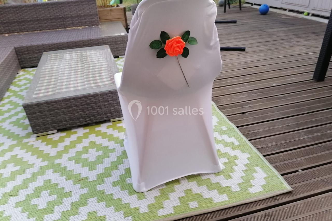 Chaise blanche décorée d'une rose orange, placée sur une terrasse en bois avec un tapis à motifs verts et blancs.