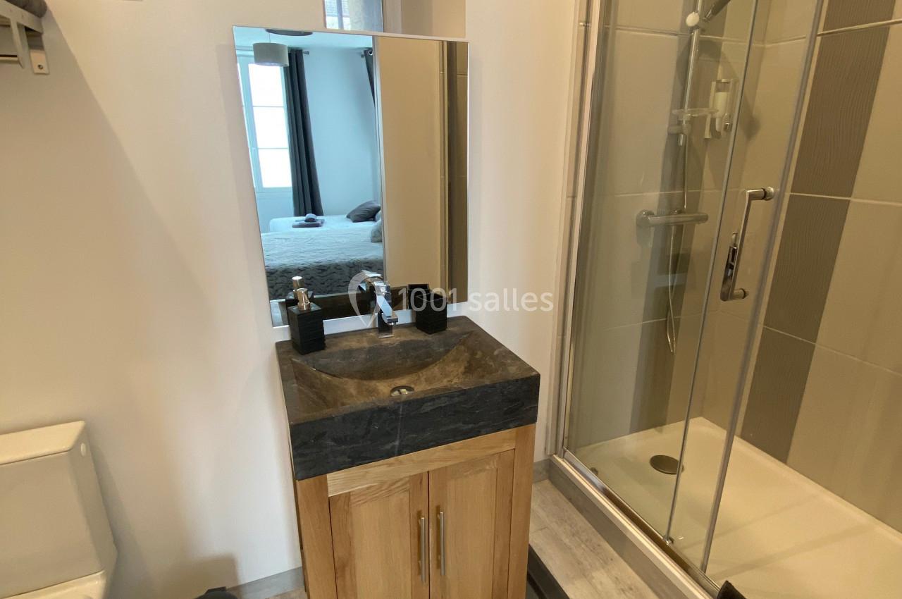 Salle de bain avec douche vitrée, lavabo sur meuble en bois, miroir, toilettes et sol en parquet clair.
