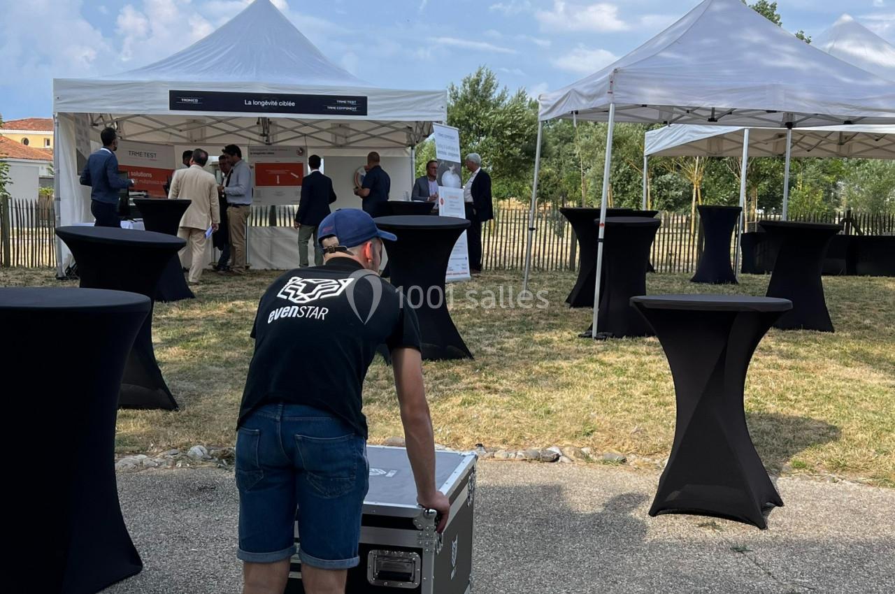 Un technicien déplace un caisson devant des tentes blanches lors d'un événement en extérieur.