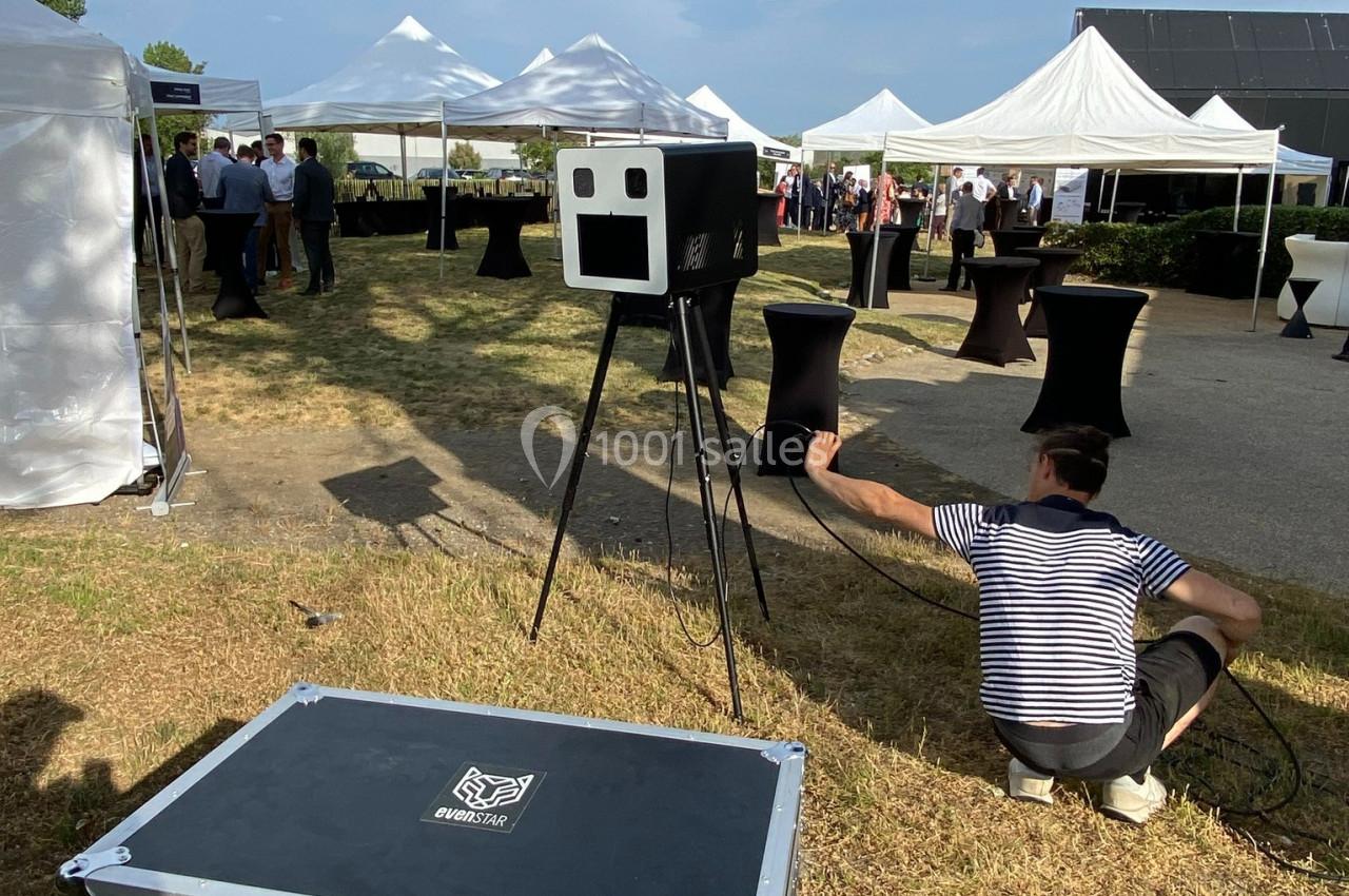 Un événement en extérieur avec des tentes blanches, un photobooth et un technicien ajustant un câble au sol.